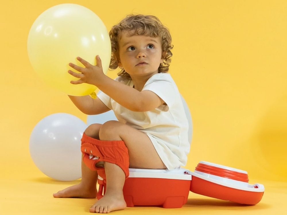 Toddler sat on potty holding a yellow balloon