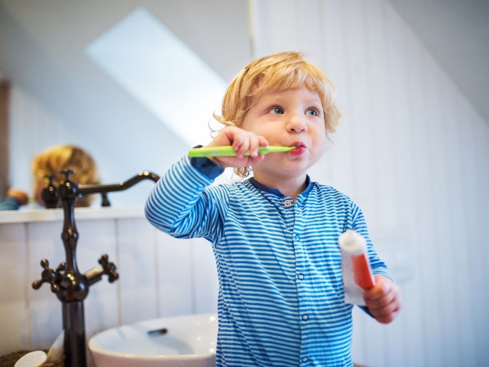 Toddler cleaning teeth with tooth brush in a bathroom