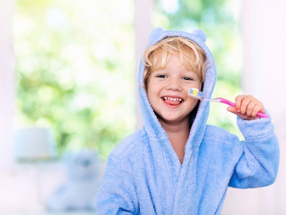 Toddler in blue dressing gown cleaning teeth with tooth brush in a bathroom