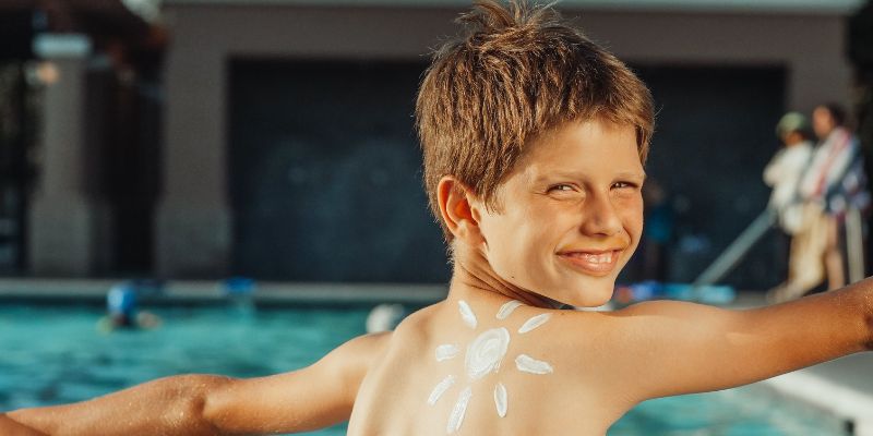 Boy by swimming pool with sunscreen on shoulder